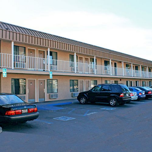 The image shows a two-story motel building with parked cars in front of it, featuring an outdoor corridor and simple architecture.