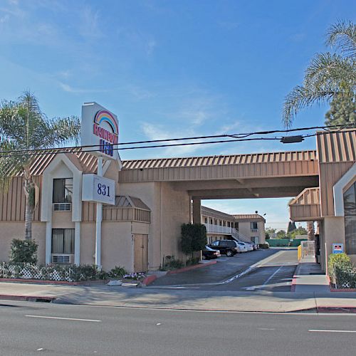 The image shows a motel with a sign displaying the number 831, palm trees, a driveway, and a clear blue sky in the background.