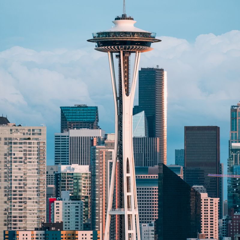 This image features the Space Needle, a famous observation tower in Seattle, with the city's skyline in the background, under a sky with scattered clouds.