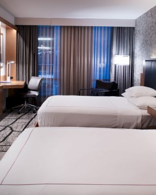A modern hotel room with two neatly made beds, a flat-screen TV, a work desk with a chair, and stylish decor and lighting.