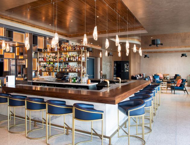 A modern bar with elegant seating, unique pendant lights, and a well-stocked liquor display behind the counter.