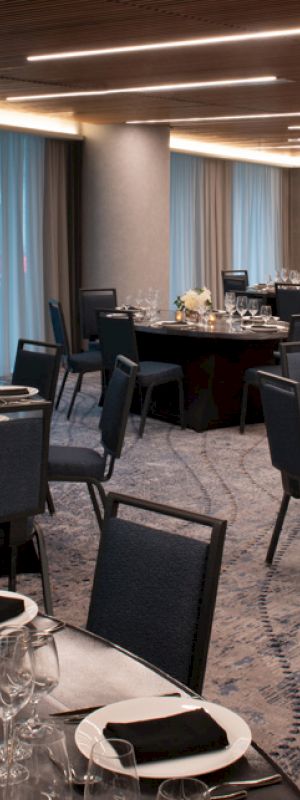The image shows a modern banquet hall with round tables set for an event. The hall features elegant lighting and decor, with chairs neatly arranged.