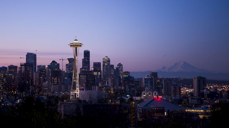 A cityscape featuring iconic towers, skyscrapers, and buildings, with a mountain in the background and the sky transitioning from dusk to night.