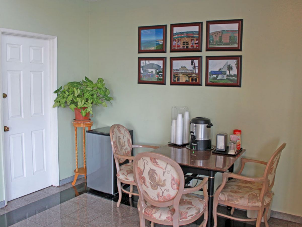 A small dining area with a table, four chairs, coffee setup, plant, and framed pictures on the wall.