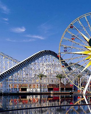 The image shows an amusement park with a large Ferris wheel featuring a familiar mouse face and a roller coaster with 