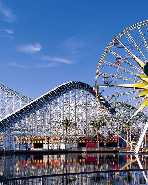 The image shows an amusement park with a large Ferris wheel featuring a familiar mouse face and a roller coaster with "Paradise Pier" signage.
